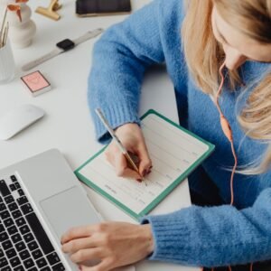 woman in blue sweater writing on her planner
